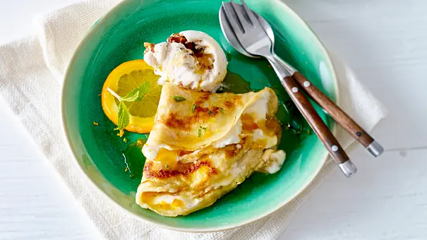 Zarter Crêpe, gefüllt mit Orangencreme, serviert mit einer Orangenscheibe und einer Kugel Eis auf einem grünen Teller. - Foto: LECKER @ Bauer Media Group