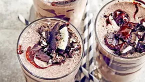 Drei Gläser cremiger Cookie & Cream Milchshake, getoppt mit zerbröselten Schokokeksen und Schokosauce, dazu gestreifte Papierstrohhalme auf einer hellen Unterlage. - Foto: LECKER @ Bauer Media Group Drei Gläser cremiger Cookie & Cream Milchshake, getoppt mit zerbröselten Schokokeksen und Schokosauce, dazu gestreifte Papierstrohhalme auf einer hellen Unterlage. - Foto: LECKER @ Bauer Media Group