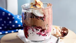 Schichtdessert im Glas mit cremiger Schokoladenmousse, Beeren, gerösteten Marshmallows und Sahne auf einem kleinen Holzbrett, daneben ein Löffel. - Foto: StockFood Foto