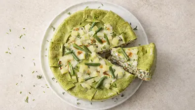 Runde Lasagne mit grünen Nudelplatten, gefüllt mit Hähnchen, grünen Bohnen und weißen Bohnen, cremig überbacken und mit frischen Kräutern bestreut, serviert auf einem weißen Teller, ein Stück herausgeschnitten. - Foto: StockFood Foto