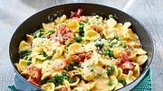 Pasta in cremiger Carbonara-Soße mit Erbsen und Schinkenstücken in einer Pfanne auf grünem Untersetzer. - Foto: House of Food / Bauer Food Experts KG