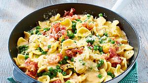 Pasta in cremiger Carbonara-Soße mit Erbsen und Schinkenstücken in einer Pfanne auf grünem Untersetzer. - Foto: House of Food / Bauer Food Experts KG