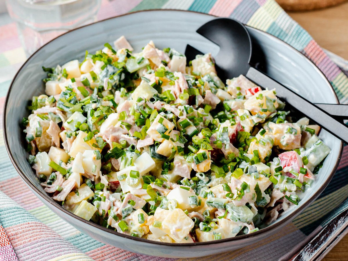 7-Tassen-Salat mit Schnittlauch in einer großen blauen Servierschüssel mit schwarzem Servierbesteck