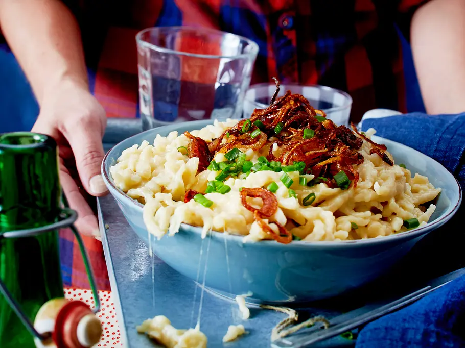 Ein blaue Schale mit Käsespätzle und selbst gemachten Röstzwiebeln, an der Seite lange Käsefäden