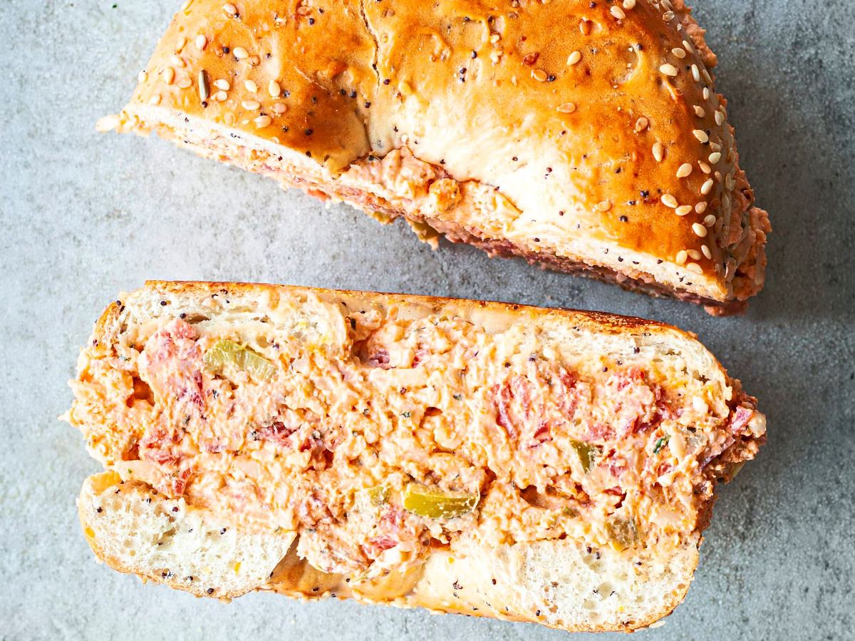 Sesambagel mit cremiger Füllung aus Tomaten, Käse und Oliven im Pizza-Style