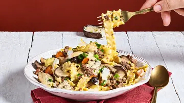 Eine Hand hebt mit einer goldenen Gabel Bandnudeln von einem Teller mit Pilzen, Gemüse, Käse und cremiger Sauce. - Foto: StockFood Studios / Meike Bergmann Eine Hand hebt mit einer goldenen Gabel Bandnudeln von einem Teller mit Pilzen, Gemüse, Käse und cremiger Sauce. - Foto: StockFood Studios / Meike Bergmann