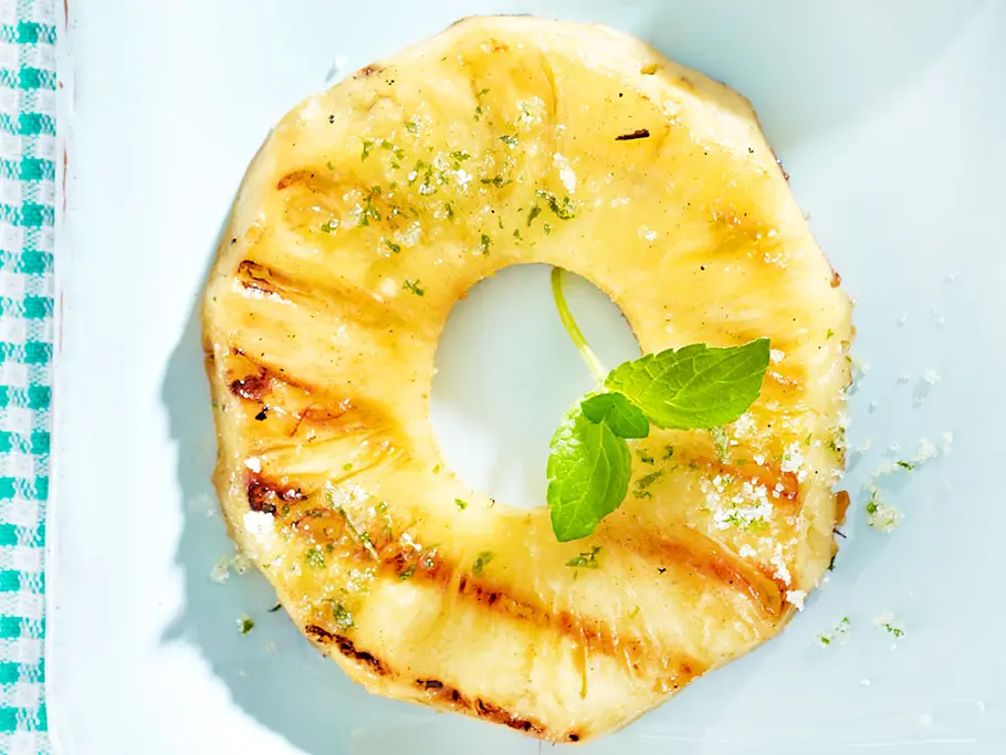 Ananas grillen Rezept Eine gegrillte Ananasscheibe mit einem Minzblättchen serviert.