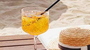 Andalö Spritz / Sanddorn Spritz in einem hohen Glas auf einem Holztisch am Strand. - Foto: Chiociolla / iStock