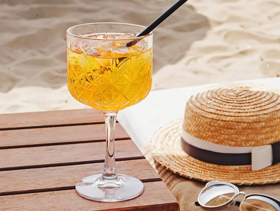 Andalö Spritz / Sanddorn Spritz Andalö Spritz / Sanddorn Spritz in einem hohen Glas auf einem Holztisch am Strand.