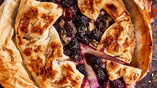 Rustikale Blätterteig-Galette, gefüllt mit gebackenem Brie und Brombeeren, serviert auf Backpapier mit einem Stück angeschnitten. - Foto: LECKER @ Bauer Media Group
