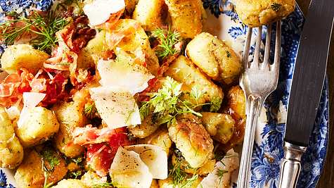 Goldbraun gebratene Ricotta-Gnocchi, serviert mit knusprigem Schinken, frischen Kräutern und groben Parmesanspänen auf einem Teller mit Blumenmuster. - Foto: LECKER @ Bauer Media Group