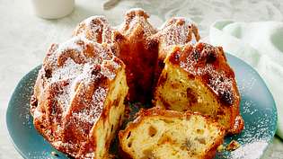Ein angeschnittener, mit Puderzucker bestäubter Apfel-Maronen-Gugelhupf auf einem türkisfarbenen Teller - Foto: LECKER @ Bauer Media Group
