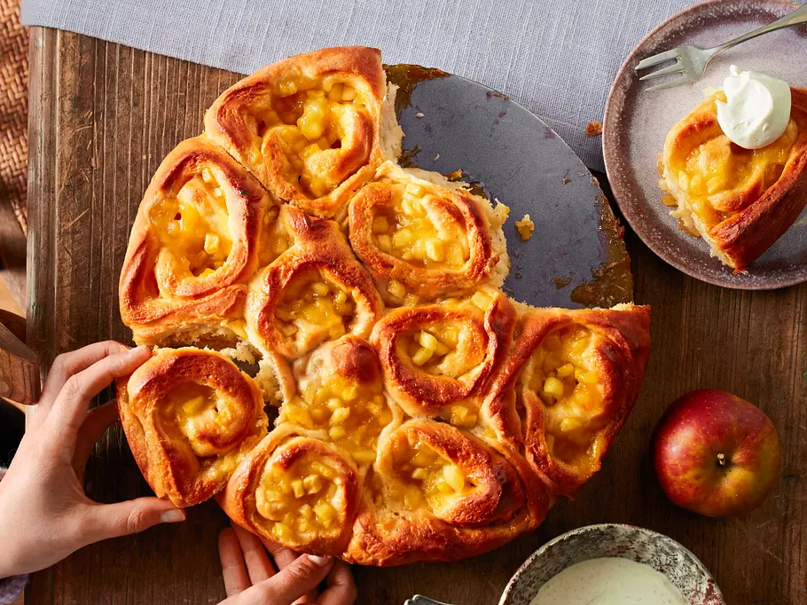 Apfel-Hefeschnecken-Kuchen Apfel-Zimtschnecken in einer Springform, daneben ein Teller mit einer einzelnen Apfel-Zimtschnecke.