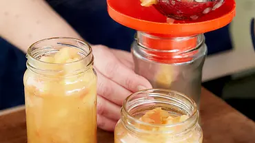 Eingekochte Äpfel werden mit Hilfe eines Trichters in 3 Gläser gefüllt. - Foto: LECKER @ Bauer Media Group Eingekochte Äpfel werden mit Hilfe eines Trichters in 3 Gläser gefüllt. - Foto: LECKER @ Bauer Media Group
