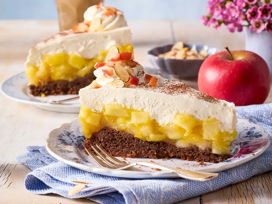 Apfeltorte mit Sahnehaube Ein Stück Apfeltorte mit Schokoboden, Kompott und Schmand-Sahnehaube auf einem Teller serviert.
