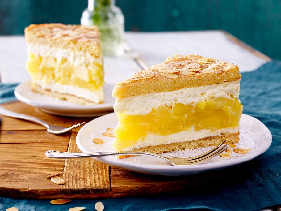 Saftige Apfelweintorte mit heller Creme und Mandelblättchen auf zwei Tellern.
