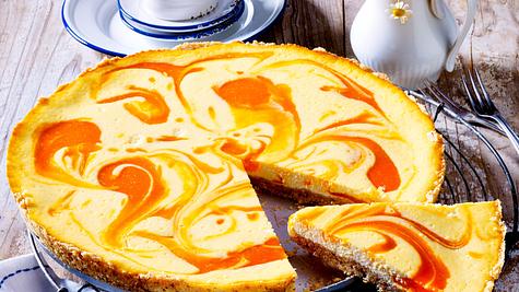 Eine runde Tarte mit gelber Ricottafüllung und orangefarbenen Aprikosenswirls liegt auf einem Gitterrost, ein Stück ist angeschnitten. - Foto: LECKER @ Bauer Media Group