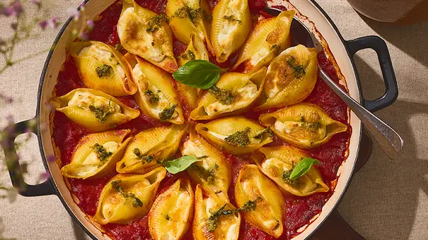 Gefüllte Pasta-Muscheln in einer runden Auflaufform, gefüllt mit cremiger Zitronen-Ricotta-Mischung, serviert auf einer Schicht Tomatensauce und garniert mit grünem Pesto und frischem Basilikum. - Foto: ITA Assolatte