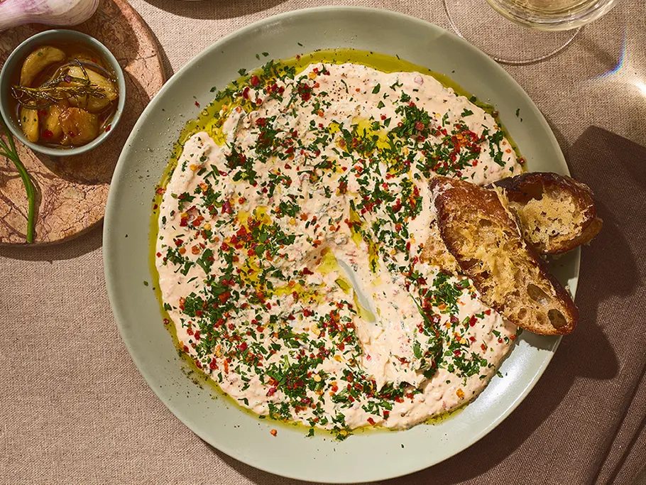 Knoblauch-Dip mit Parmigiano Reggiano & Brot Cremiger Knoblauch-Dip mit Olivenöl, frischen Kräutern und Parmigiano Reggiano, serviert auf einem runden Teller mit knusprigem Brot.