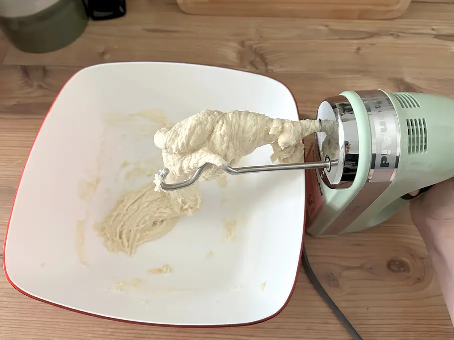 Topshot von einer Rühschüssel mit Hefeteig, der sich auf einem der Knethaken vom KitchenAid-Handmixer bis zur Gehäuseöffnung aufgewickelt hat