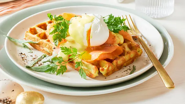 Herzhafte Avocado-Waffeln, belegt mit Räucherlachs, einem pochierten Ei, cremiger Sauce Hollandaise und frischen Kräutern, serviert auf einem weißen Teller mit goldener Gabel auf einem hellen, gedeckten Tisch. - Foto: LECKER @ Bauer Media Group Herzhafte Avocado-Waffeln, belegt mit Räucherlachs, einem pochierten Ei, cremiger Sauce Hollandaise und frischen Kräutern, serviert auf einem weißen Teller mit goldener Gabel auf einem hellen, gedeckten Tisch. - Foto: LECKER @ Bauer Media Group