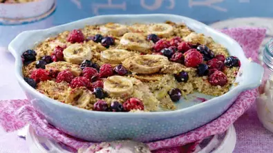 Eine hellblaue Auflaufform gefüllt mit einer gebackenen Masse aus Haferflocken, Milch, Honig, TK-Beeren und Banane - Foto: LECKER @ Bauer Media Group / KI-optimiert