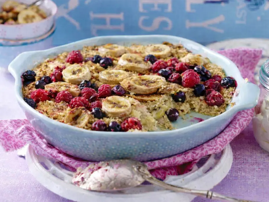 Eine hellblaue Auflaufform mit einer gebackenen Masse aus Haferflocken, Milch, Honig, TK-Beeren und Banane