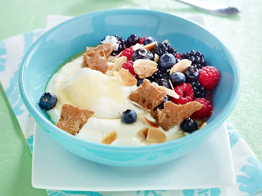 Beeren-Knusper-Quark Quark in einer blauen Schale mit Beeren und Knäckebrot-Crunch
