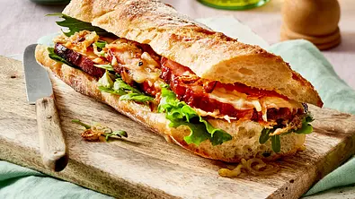Ein üppig belegtes, rustikales Baguette auf einem Holzbrett - Foto: LECKER @ Bauer Media Group