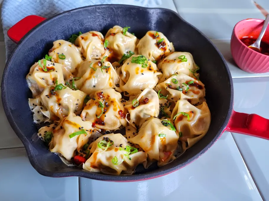 Blanket Dumplings in der Pfanne mit schwarzem Sesam und Frühlingszwiebeln garniert.