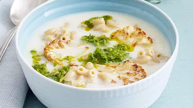 Eine hellblaue Schüssel mit Blumenkohl-Käsesuppe und Hörnchennudeln. Garniert mit Pesto und Blumenkohlstücken. - Foto: Stellmach, Peter