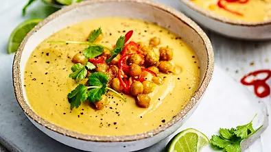 Eine Schale mit goldgelber cremiger Blumenkohlsuppe mit Kichererbsen-Topping, Chili-Scheiben und Kräutern - Foto: Are Media Syndication 