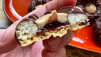 Ein halbiertes Bueno-Plätzchen mit Waffelboden, Haselnussfüllung und Geleefüllung wird von einer Hand in die Kamera gehalten - Foto: LECKER @ Bauer Media Group / Katharina Klieme