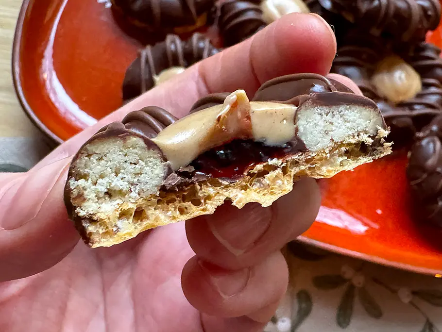 Bueno-Plätzchen mit Geleefüllung Ein halbiertes Bueno-Plätzchen mit Geleefüllung wird von einer Hand in die Kamera gehalten