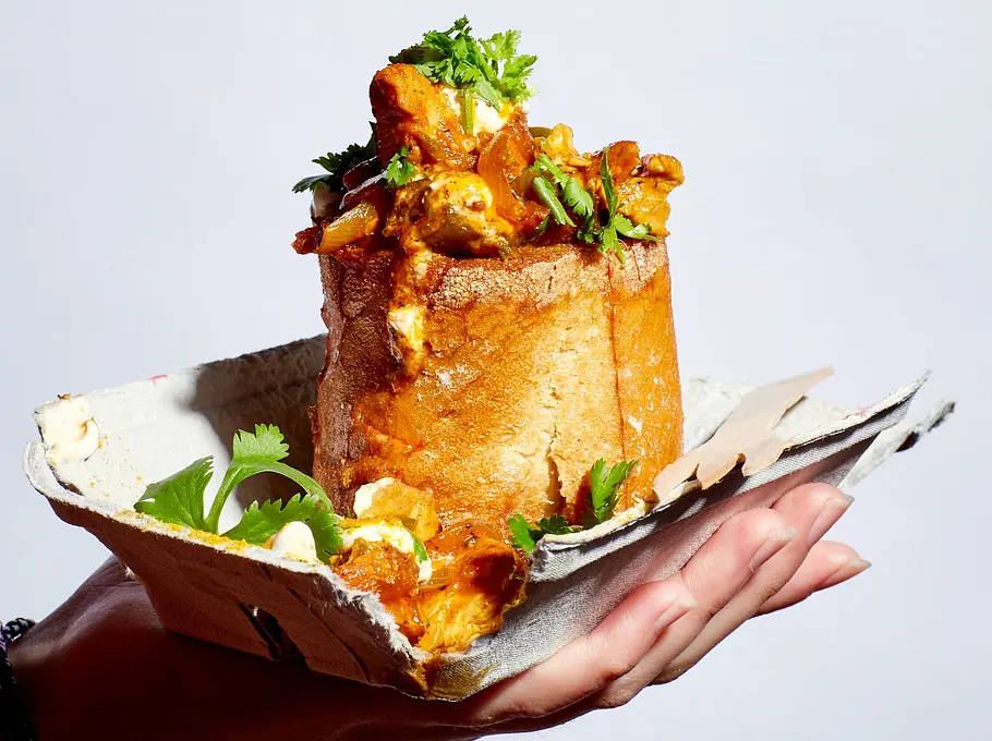 Bunny Chow Rezept Ausgehöhltes Weißbrot, gefüllt mit würzigem Curry und frischem Koriander, serviert auf einem Stück Papier in der Hand gehalten.