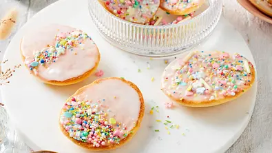 Mehrere Amerikaner in Ei-Form sind mit Zuckerguss und bunten Streusel verziert. - Foto: LECKER @ Bauer Media Group