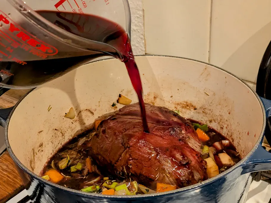 Ein großes Stück Rindfleisch zwischen geschnittenem Gemüse wird mit Rotwein übergossen.