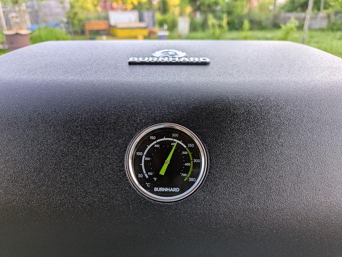 burnhard-gasgrill-wayne-deckelthermometer Das im Deckel eines Burnhard Grills eingebaute Thermometer, das die Temperatur anzeigt, im Hintergrund ist ein Garten zu sehen.