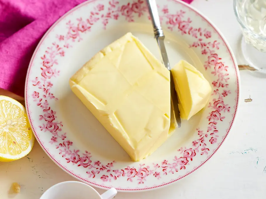 Butter auf Vorrat kaufen Ein großes Stück Butter liegt auf einem weißen Teller, der am Rand mit pinken Blumen verziert ist.