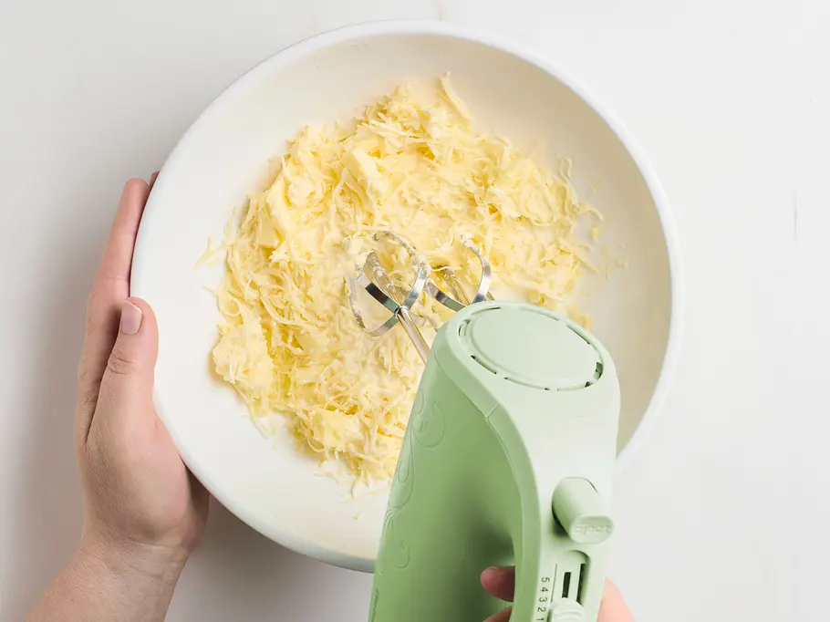 Butter schaumig schlagen Butter wird mit einem Handrührgerät in einer weißen Schüssel schaumig geschlagen.