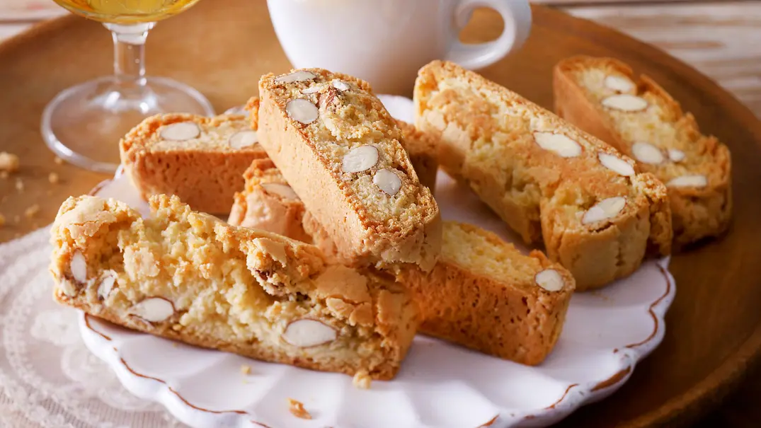 Goldbraune Cantuccini mit ganzen Mandeln liegen auf einem weißen Teller. Im Hintergrund ist eine gefüllte Espressotasse und ein Glas Vin Santo zu sehen. - Foto: LECKER @ Bauer Media Group Goldbraune Cantuccini mit ganzen Mandeln liegen auf einem weißen Teller. Im Hintergrund ist eine gefüllte Espressotasse und ein Glas Vin Santo zu sehen. - Foto: LECKER @ Bauer Media Group