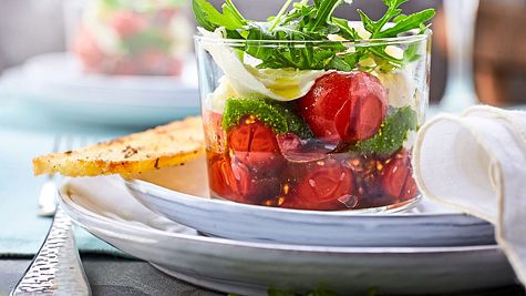 Caprese im Glas mit Kirschtomaten, Mozzarella, Pesto und frischem Rucola, serviert mit geröstetem Brot auf einem gedeckten Teller. - Foto: House of Food / Bauer Food Experts KG