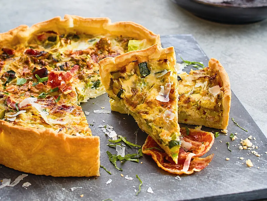 Carbonara-Quiche Aufgeschnittene Quiche auf einer schwarzen Platte, zwei Stücke liegen angeschnitten aufeinander.