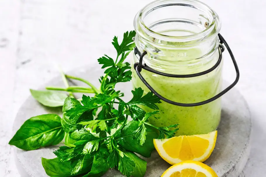Grünes Tahin-Kräuter-Dressing im Glas mit frischen Kräutern und Zitronenspalten.