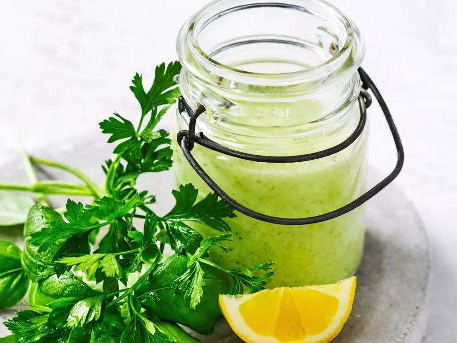 Grünes Tahin-Kräuter-Dressing im Glas mit frischen Kräutern und Zitronenspalten