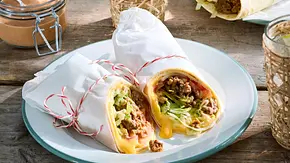 Zwei Wraps in weißem Brotpapier umhüllt auf einem runden Teller auf einem Holztisch.  - Foto: LECKER @ Bauer Media Group