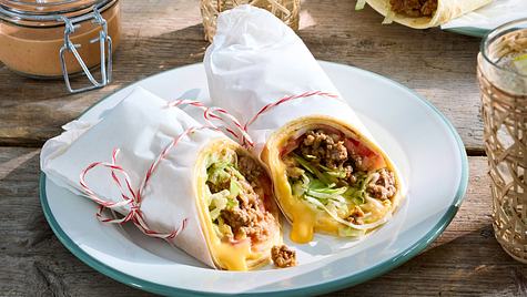 zwei Wraps in weißem Brotpapier umhüllt auf einem runden Teller auf einem Holztisch.  - Foto: House of Food / Bauer Food Experts KG