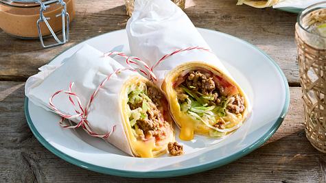 zwei Wraps in weißem Brotpapier umhüllt auf einem runden Teller auf einem Holztisch.  - Foto: House of Food / Bauer Food Experts KG