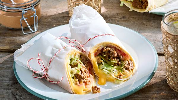 Zwei Wraps in weißem Brotpapier umhüllt auf einem runden Teller auf einem Holztisch.  - Foto: House of Food / Bauer Food Experts KG