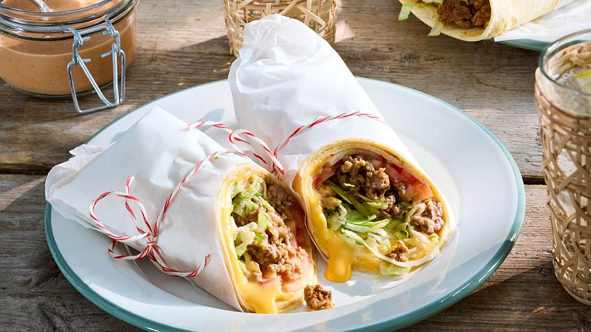 Zwei Wraps in weißem Brotpapier umhüllt auf einem runden Teller auf einem Holztisch.  - Foto: House of Food / Bauer Food Experts KG